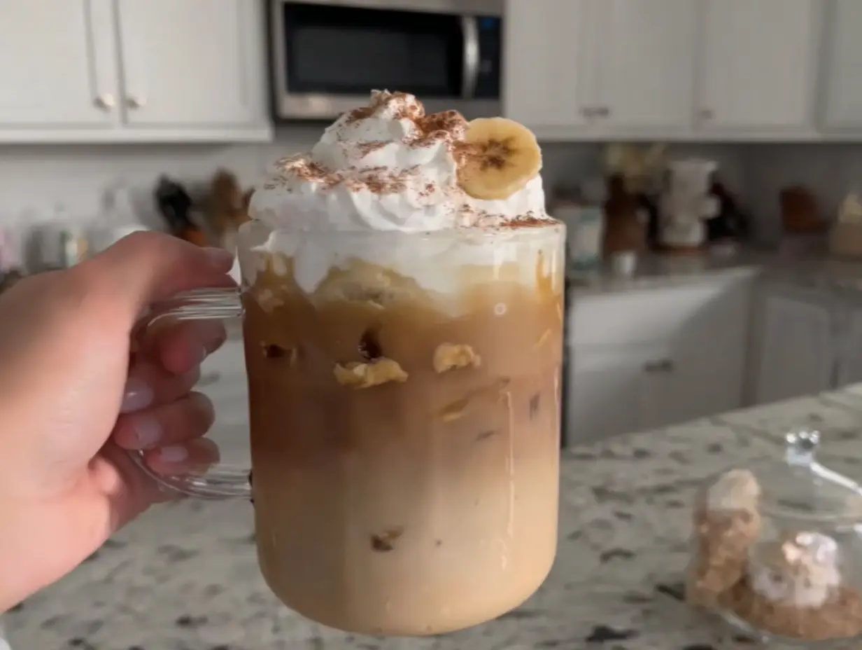 Homemade Dutch Bros Banana Bread Latte with whipped cream and banana slice held in a glass mug