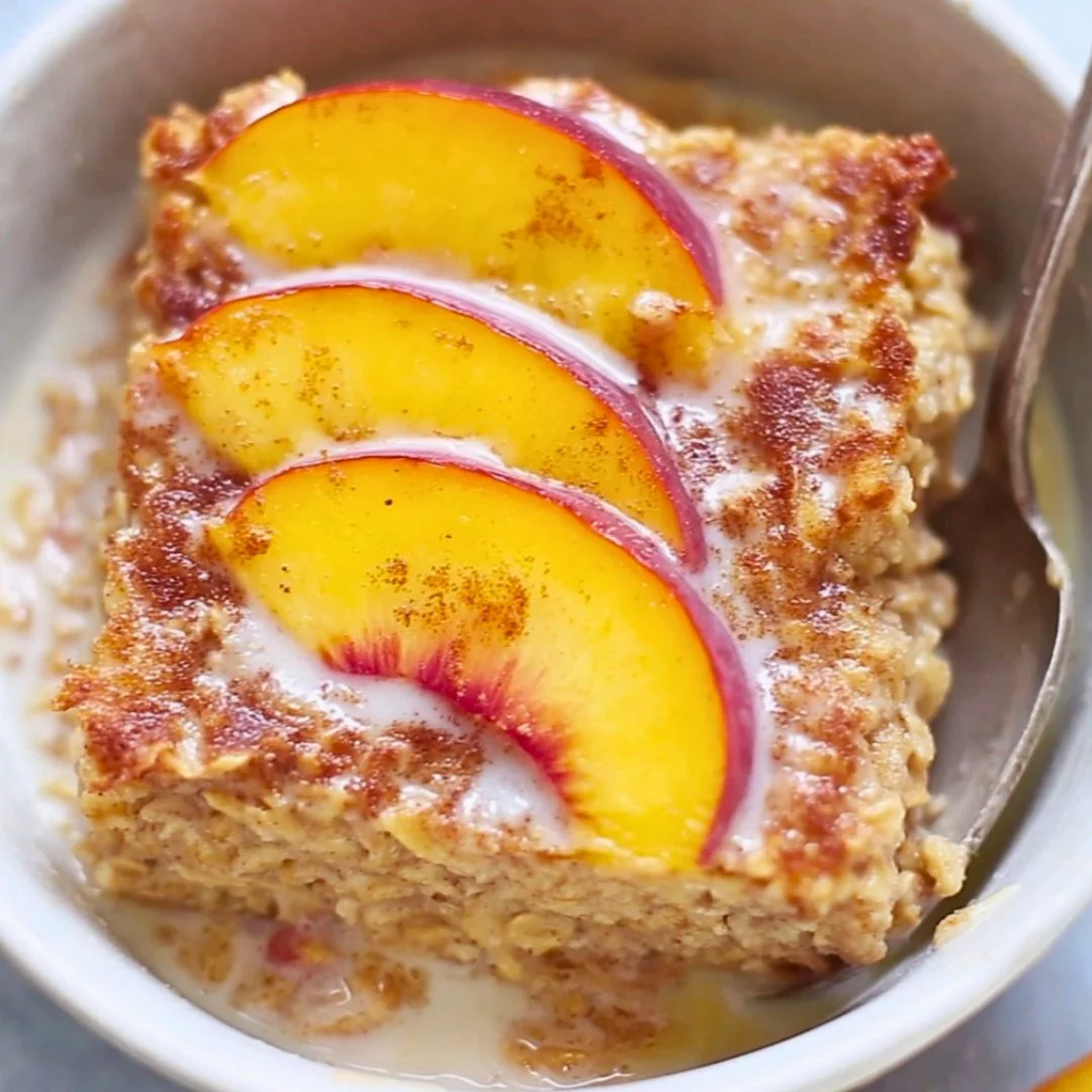 Baked peach oatmeal topped with fresh peaches and nuts in a bowl